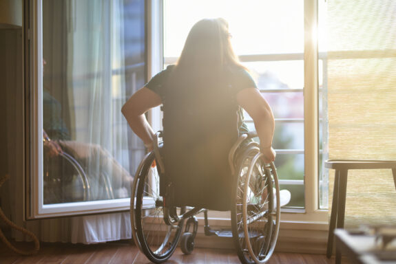 Woman in wheelchair in front of open window